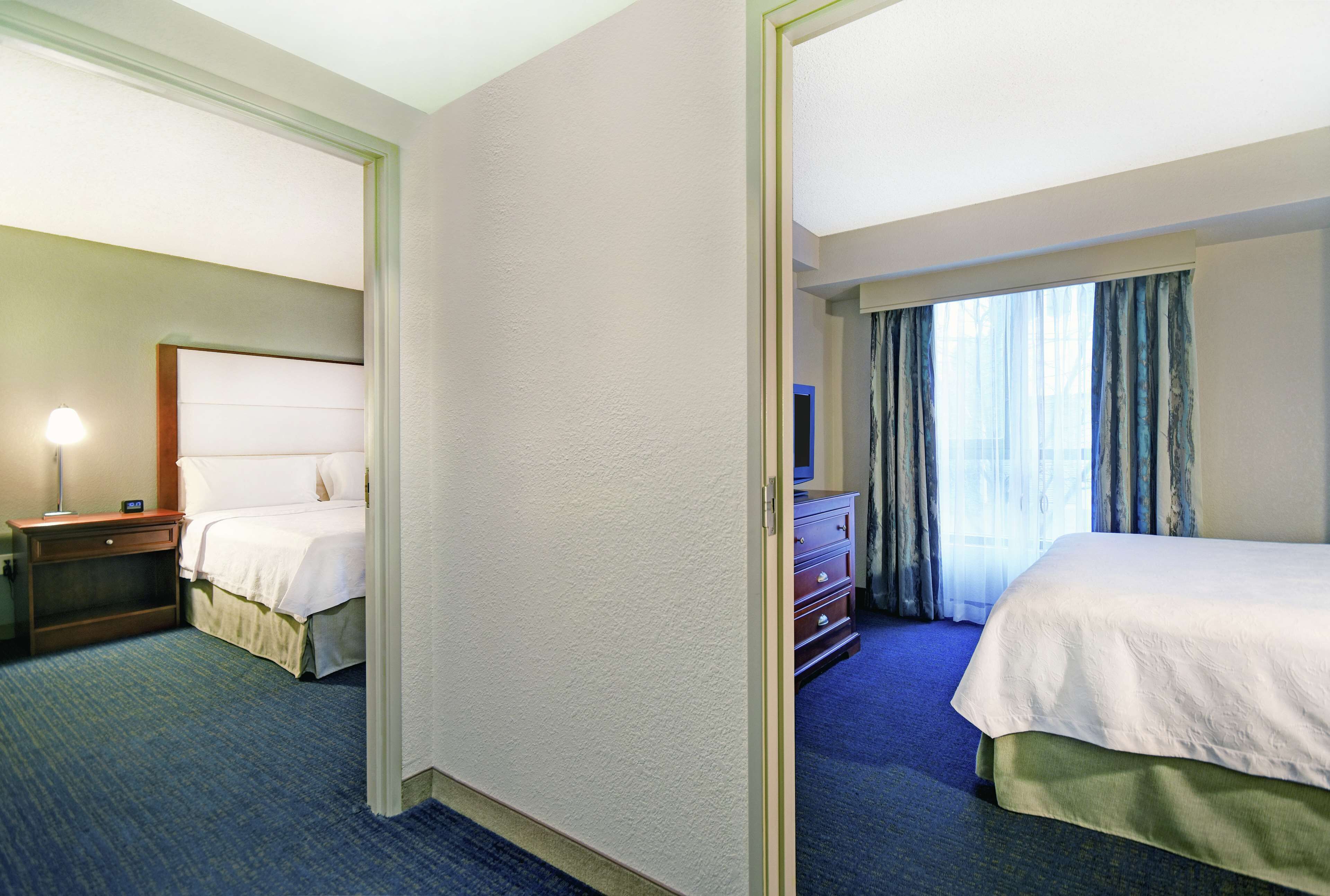 Ein Hotelzimmer mit einem großen Bett, einem Nachttisch mit Lampe, einem Schminktisch und einem Fenster mit Vorhängen.