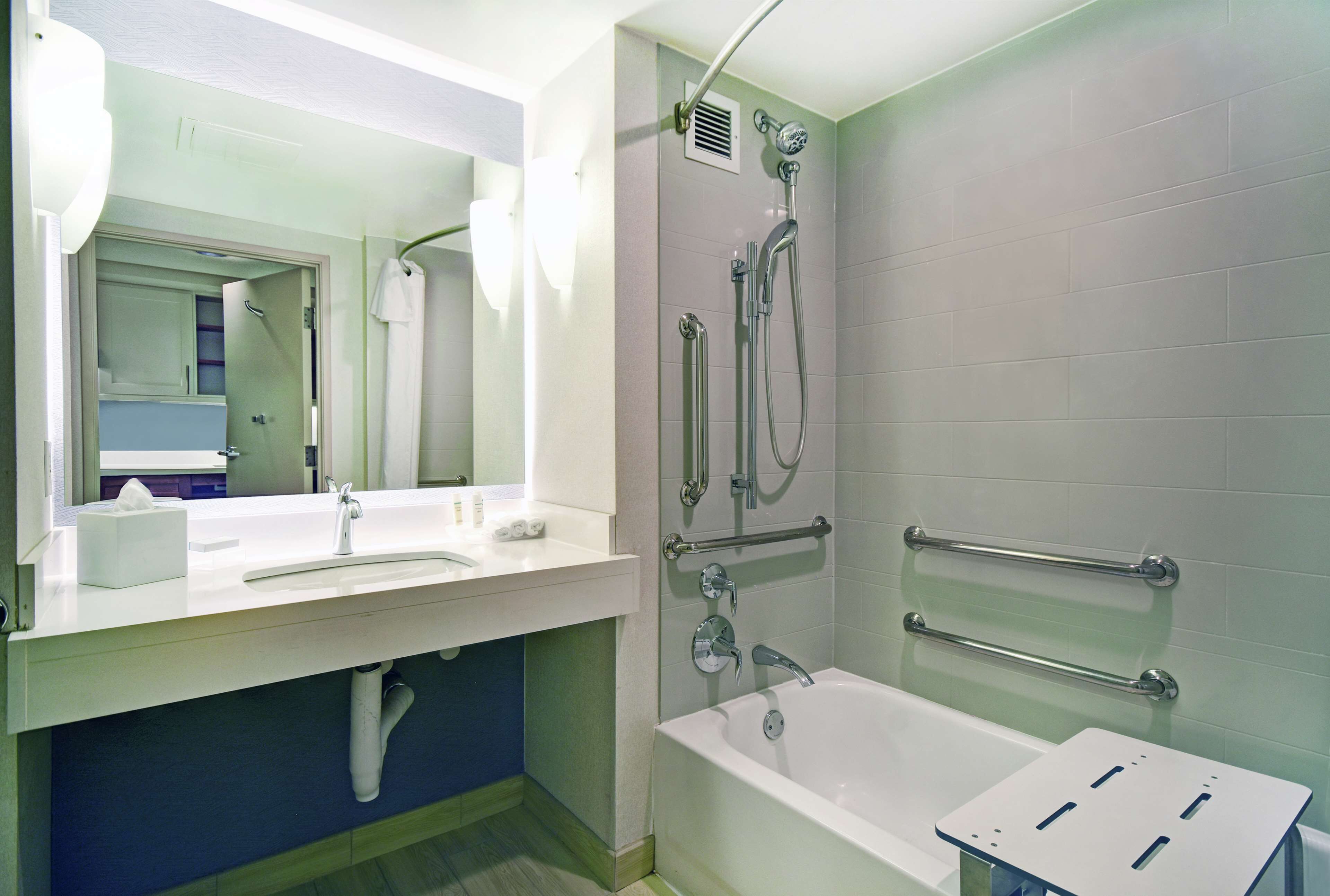 A modern bathroom with a white sink, mirror, and bathtub. There are grab bars installed near the bathtub for safety.