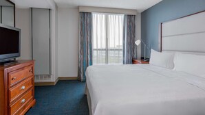 Een hotelkamer met een bed, een tv op een dressoir, een lamp en een raam met gordijnen.