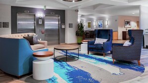 Een moderne lobby met een blauwe bank, een gestreept fauteuil, een ronde salontafel en een groot blauw-wit vloerkleed.