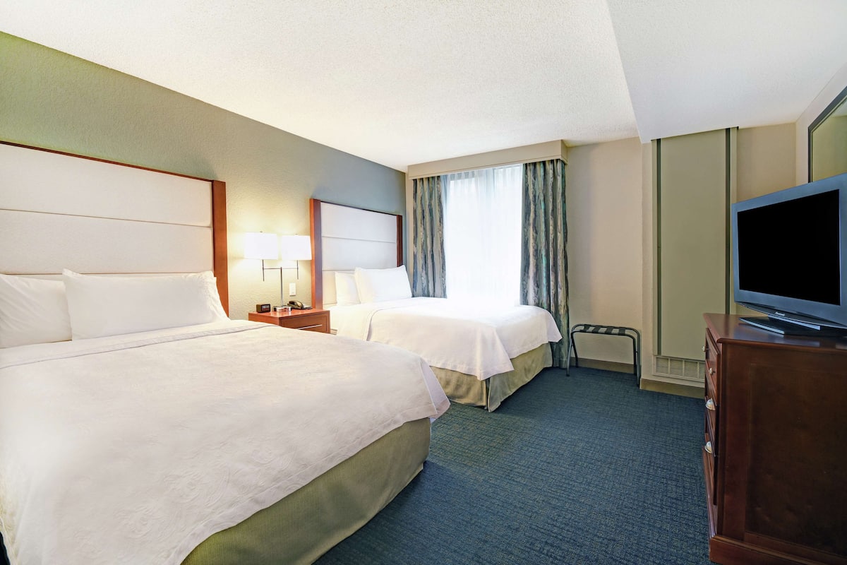 A hotel room with two beds, a television, a desk, and a chair.