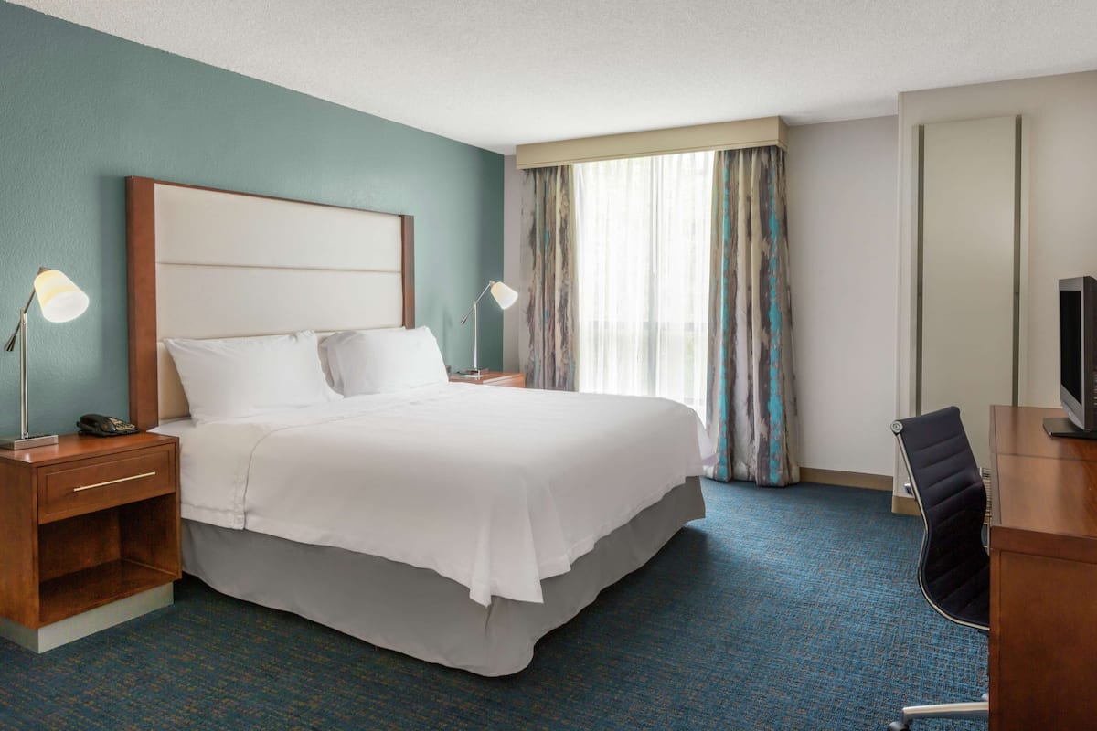 A hotel room with a large bed, bedside tables with lamps, a desk with a chair, and a television.