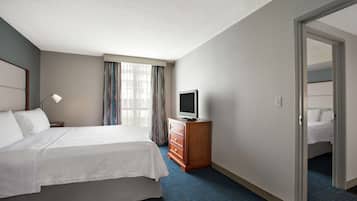 Hotellihuone, jossa on suuri sänky, televisio puukehikossa ja ovi, joka johtaa toiseen huoneeseen.