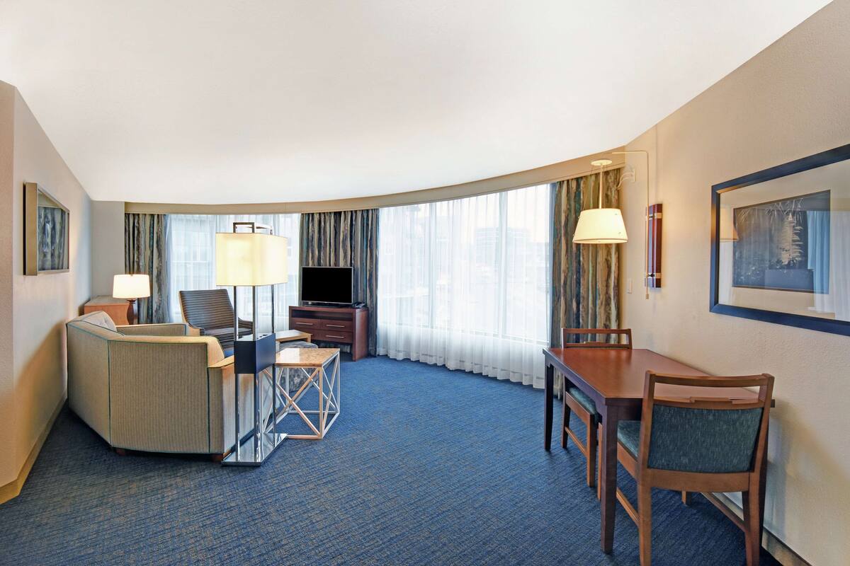 A hotel room with a curved layout, a television, a desk with a chair, and a dining area with a table and chairs.
