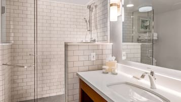 Un baño moderno con cabina de ducha de vidrio, lavabo blanco con mueble de madera y un espejo grande.