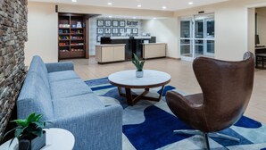 A modern hotel lobby with a reception desk, a blue sofa, a brown chair, and a round table with a plant. - Garner Hotel Macon West by IHG (Macon)