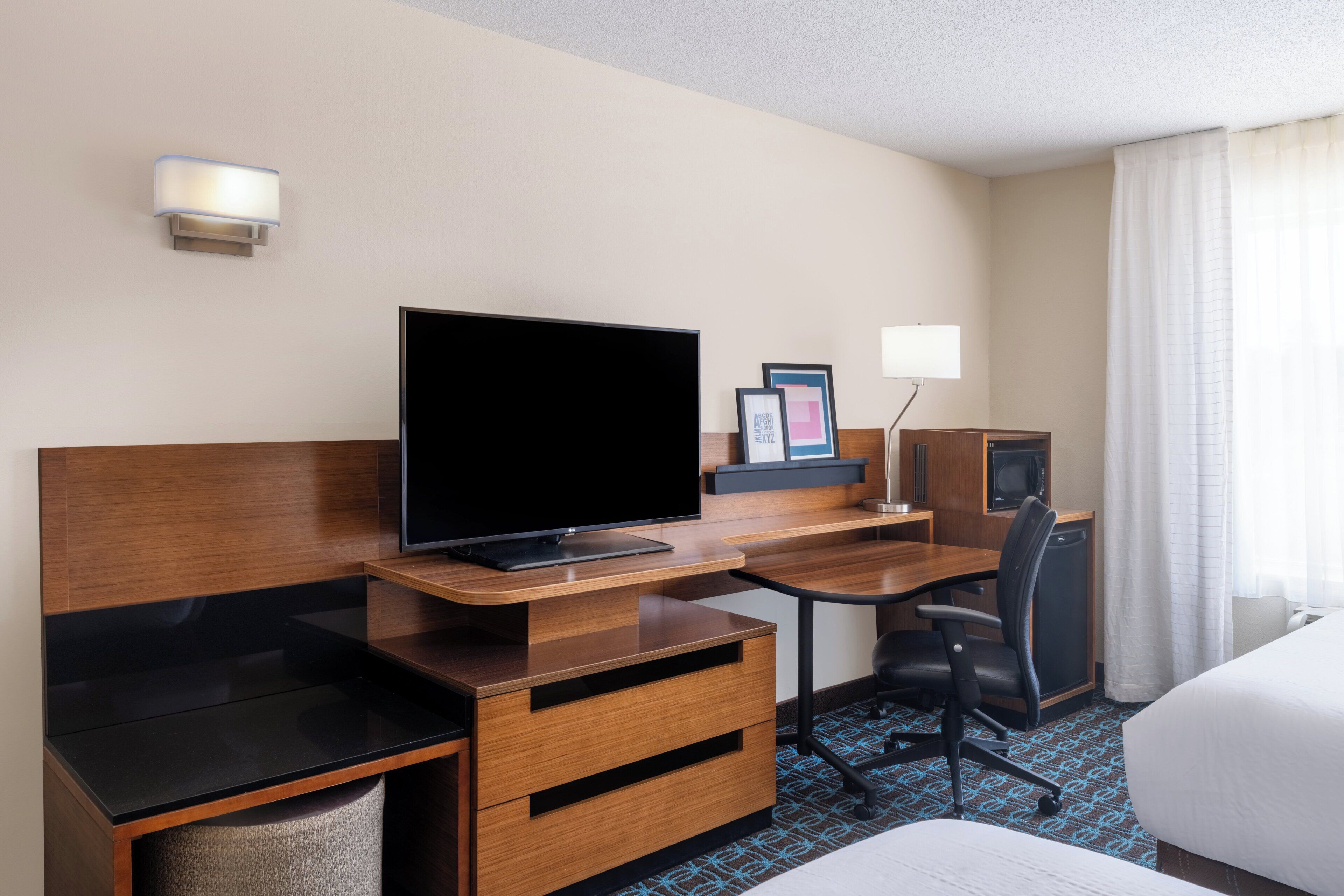 Een hotelkamer met een flatscreen televisie, een houten bureau, een stoel en een bed.