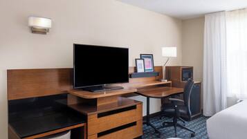 Een hotelkamer met een flatscreen televisie, een houten bureau, een stoel en een bed.