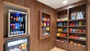 A refrigerated section with beverages and snacks, wooden shelving with various packaged goods, and a tiled floor. - Garner Hotel Macon West by IHG (Macon)
