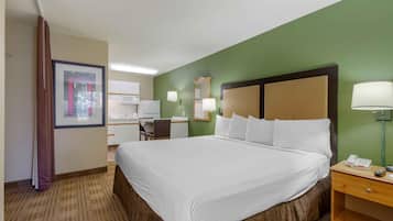 Habitación de hotel con una cama grande, un escritorio, una silla, un espejo y una mesita de noche con lámpara.