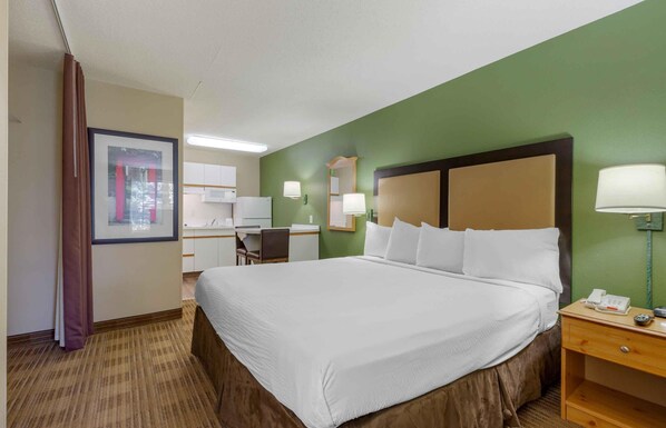 A hotel room with a large bed, a desk, a chair, a mirror, and a nightstand with a lamp.