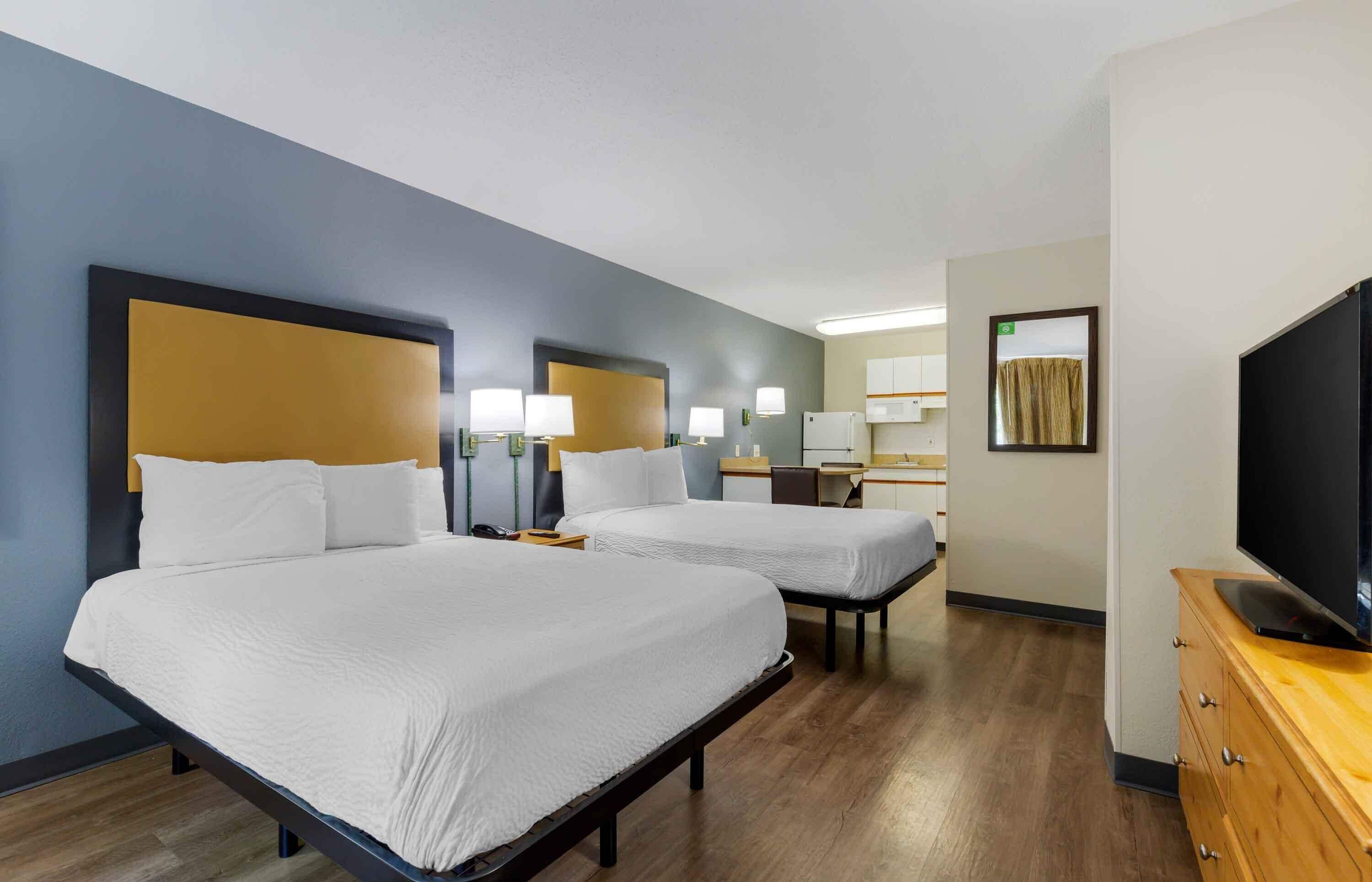 A hotel room with two beds, a TV, a desk, and a mirror.
