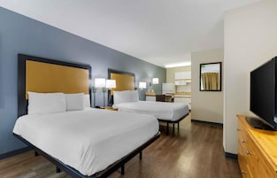 Habitación de hotel con dos camas, televisión, escritorio y espejo.