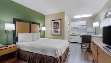 A hotel room with a bed, bedside tables, a desk, a chair, a television, and a kitchenette.