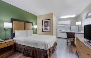 Habitación de hotel con cama, mesitas de noche, escritorio, silla, televisor y kitchenette.