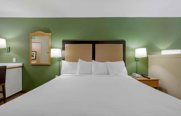 A hotel room with a large bed, two bedside lamps, a nightstand with a phone, and a mirror on the wall.