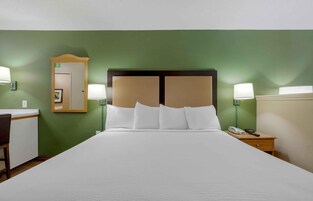 Una habitación de hotel con una cama grande, dos lámparas de noche, una mesita de noche con teléfono y un espejo en la pared.