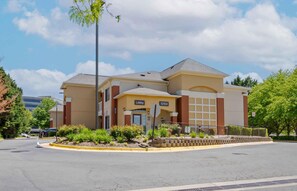 A multi-story hotel with a prominent lobby entrance, a parking lot, and a landscaped area with shrubs. - Extended Stay America Suites Washington DC Fairfax Fair Oaks (Fairfax)