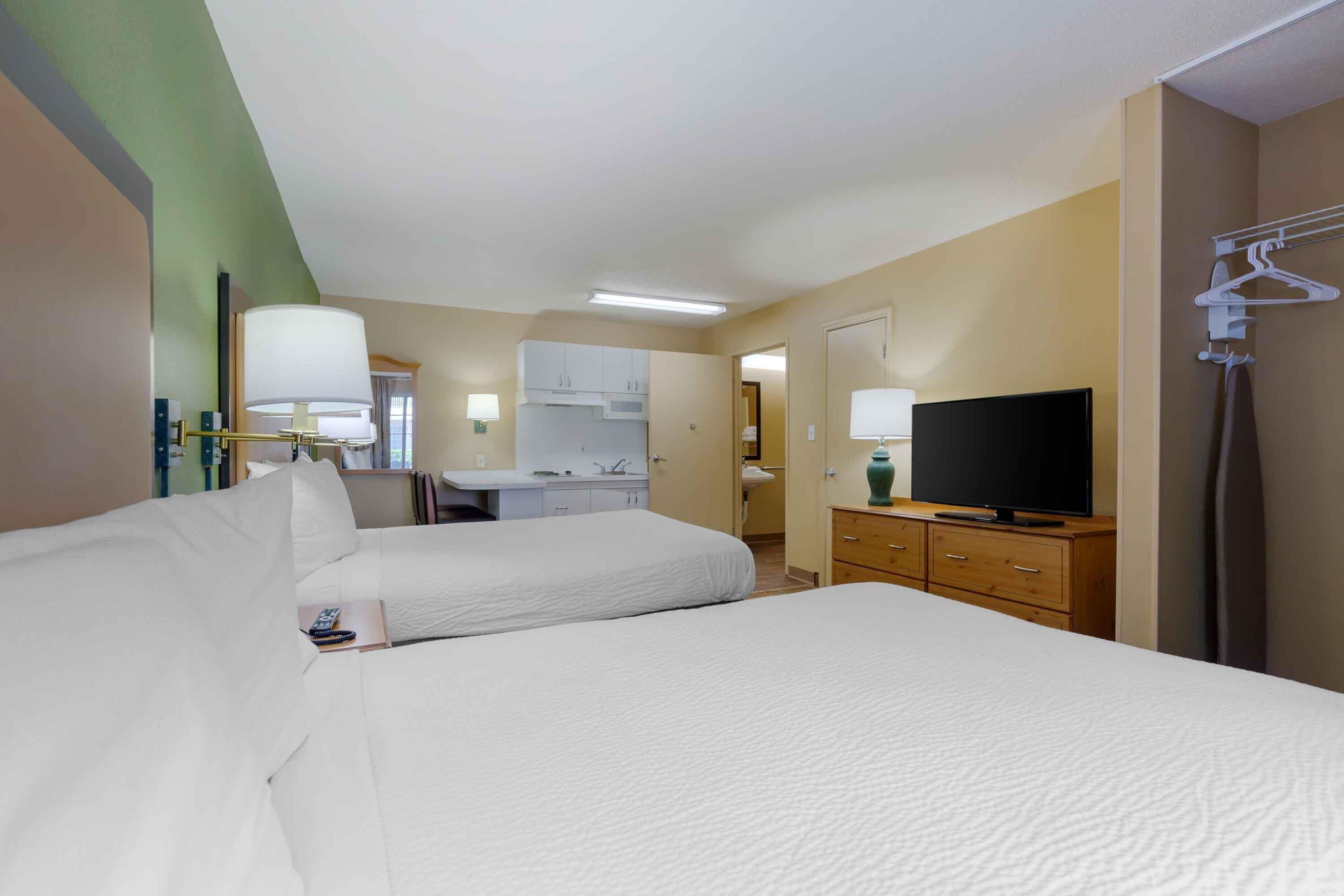 Habitación de hotel con dos camas, una televisión, un escritorio con una silla y un baño visible a través de una puerta abierta.