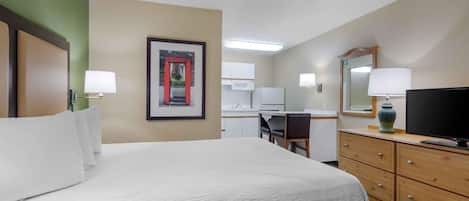 Una habitación de hotel con cama, escritorio, silla, televisión y espejo.