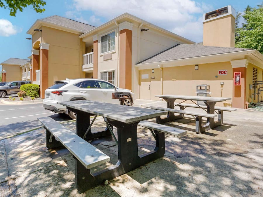 Un estacionamiento con un auto blanco, mesas de picnic y un edificio con un letrero que dice 'FDC'.