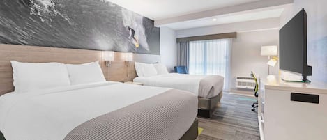 A hotel room with two beds, a large abstract painting on the wall, a desk with a computer, and a window with curtains.