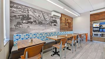 A restaurant with wooden tables and benches, a mural on the wall, and a blue and white patterned backsplash.