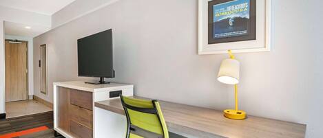 Une chambre d’hôtel équipée d’un bureau, d’une télévision, d’une affiche de film encadrée et d’une lampe.