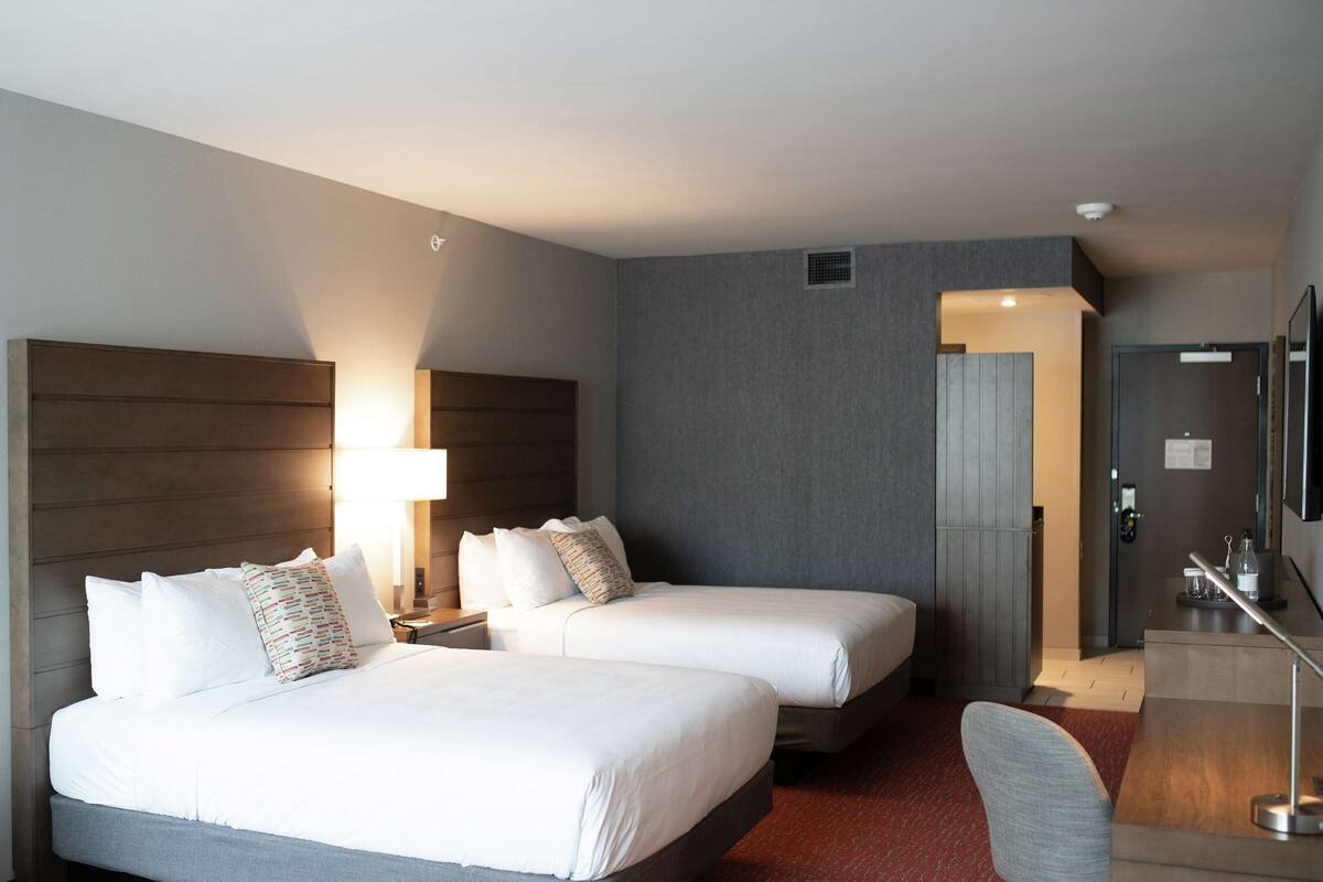 Ein Hotelzimmer mit zwei Betten, einem Schreibtisch, einem Stuhl, einer Lampe und einer Tür.