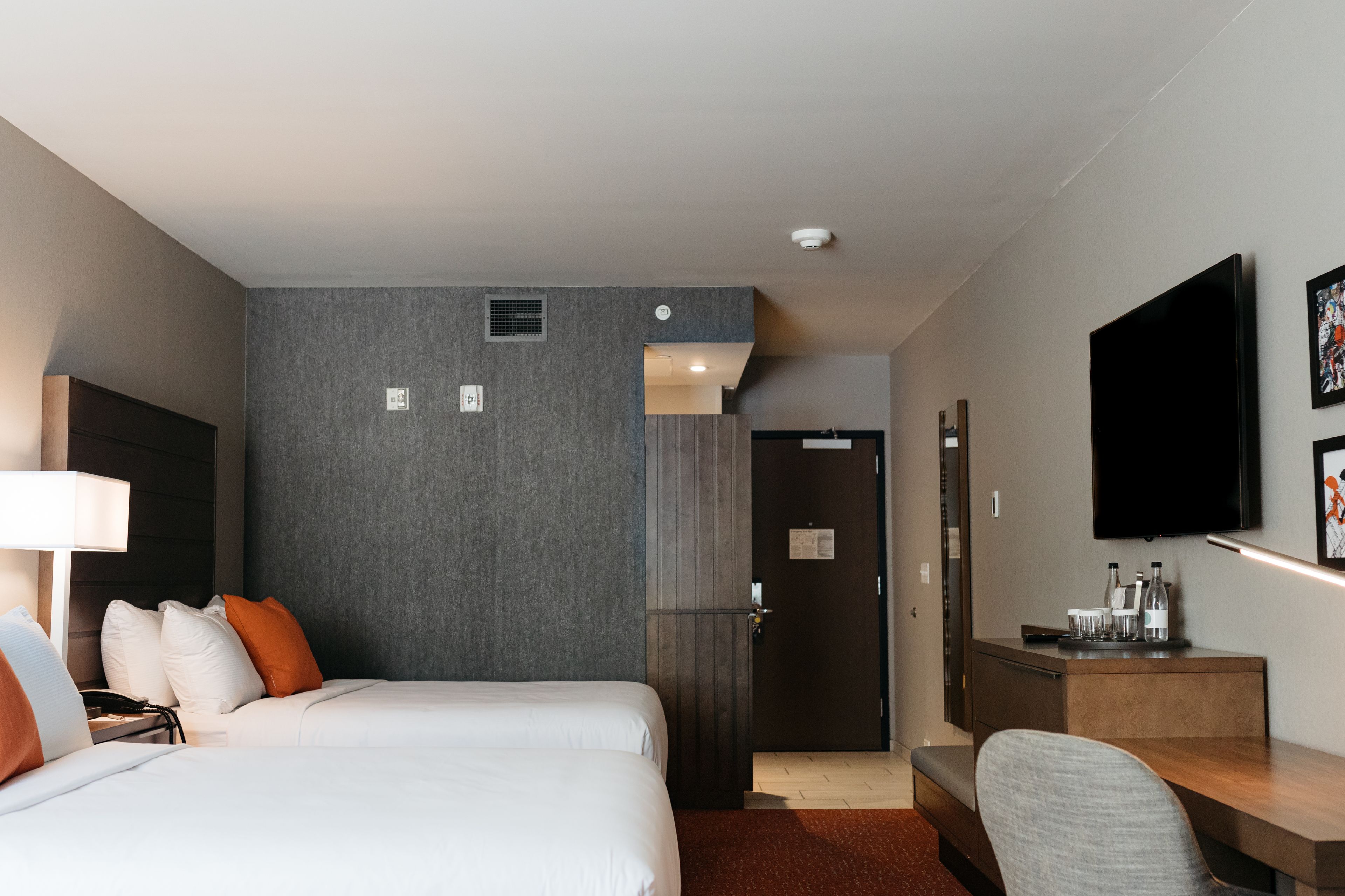 A hotel room with two beds, a desk, a TV, and a door leading to a bathroom.