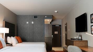 A hotel room with two beds, a desk, a TV, and a door leading to a bathroom.