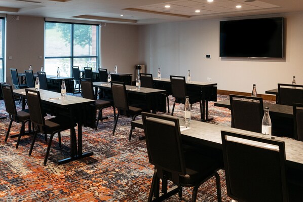 A conference room with multiple tables and chairs, a large flat-screen TV, and a carpeted floor. - Revel Hotel Des Moines Urbandale, Tapestry Collection by Hilton (Urbandale)