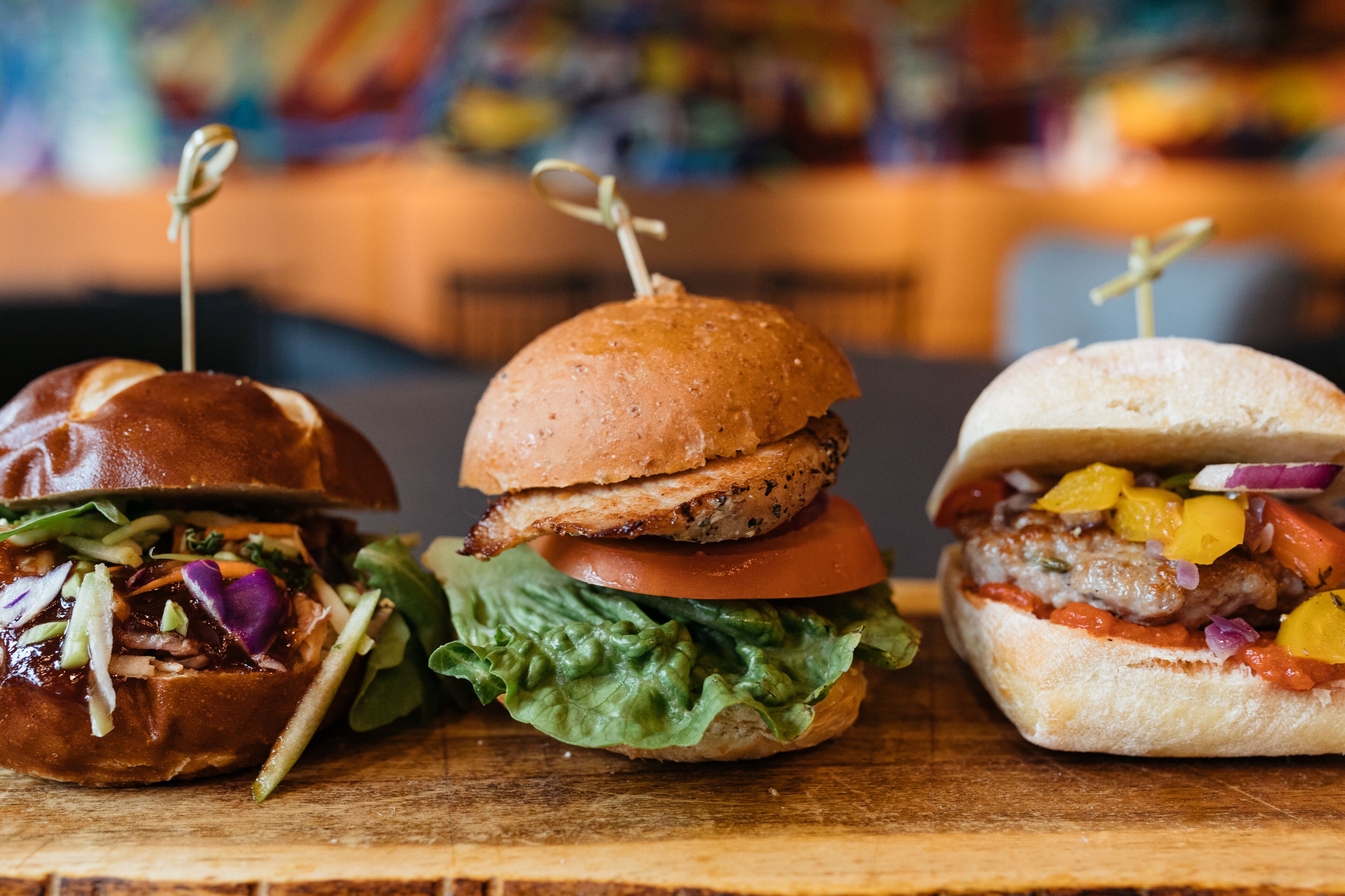 Three burgers on a wooden board.
