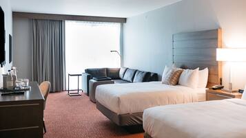 A hotel room with two beds, a desk, a chair, a sofa, and a large window with curtains.