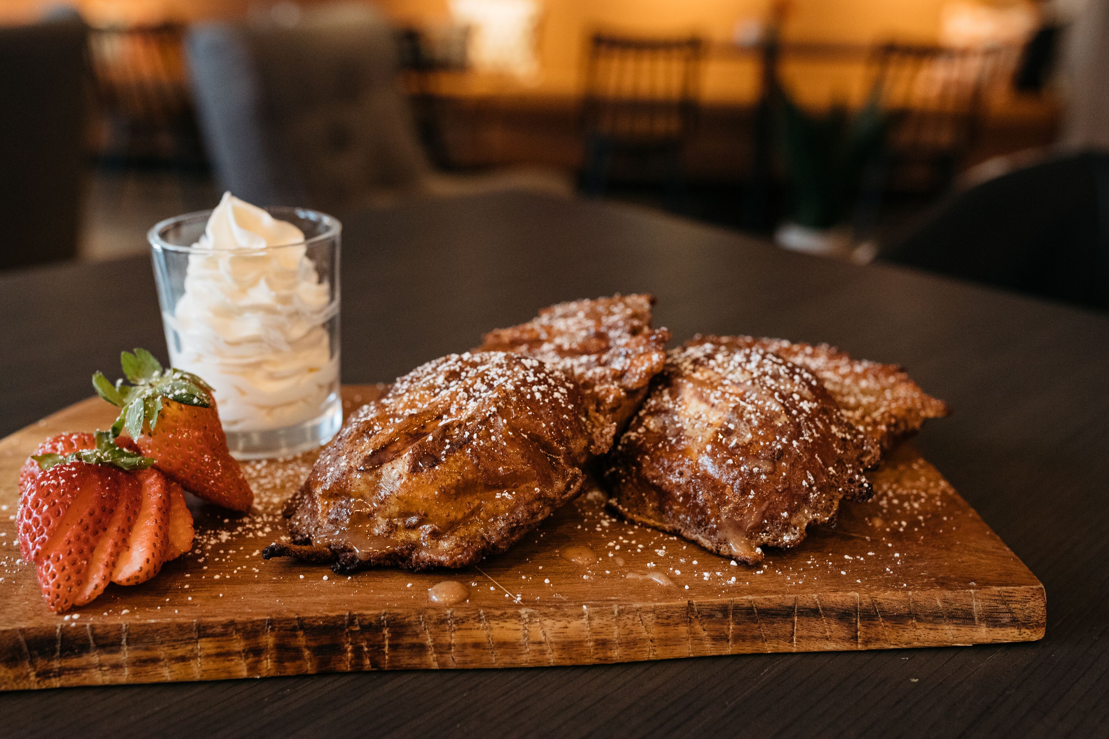 Une planche en bois garnie de pâtisseries et un verre de crème fouettée, le tout accompagné d’une fraise.