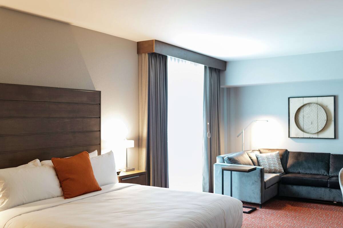 Ein Hotelzimmer mit einem großen Bett, einer Schlafcouch, einem Schreibtisch und einem Wandbild.