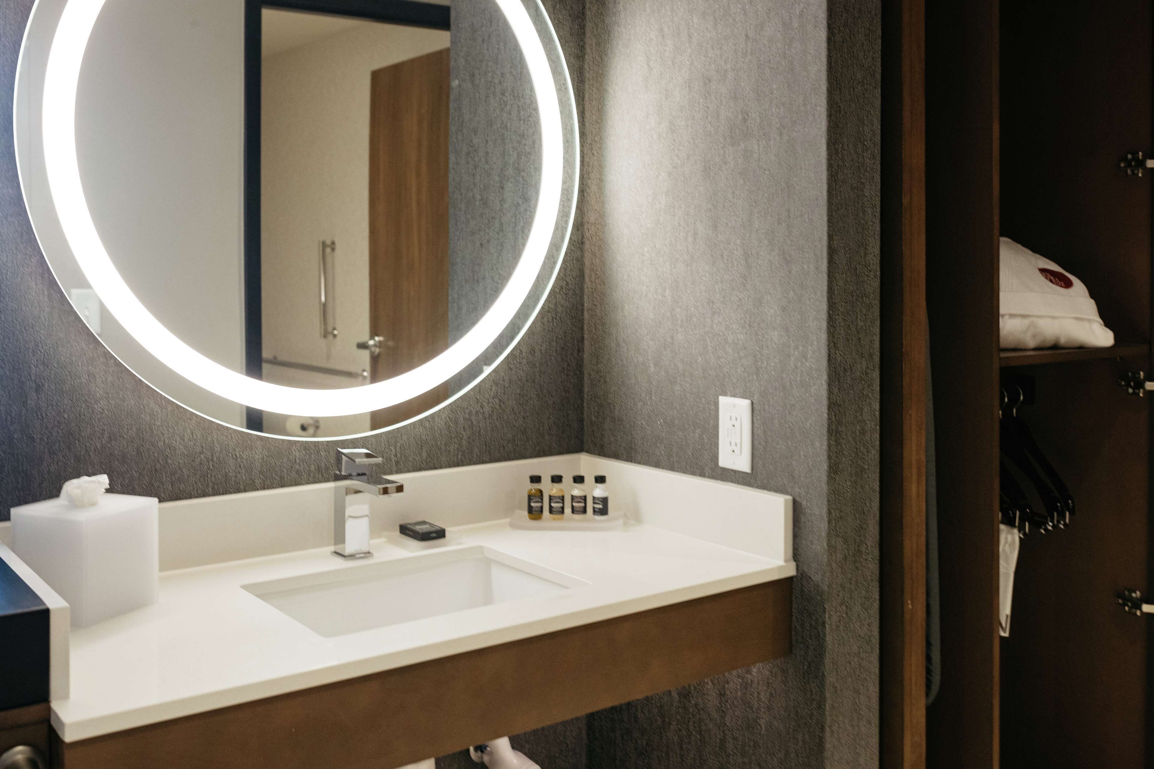 A modern bathroom with a round mirror, white sink, and toiletries.
