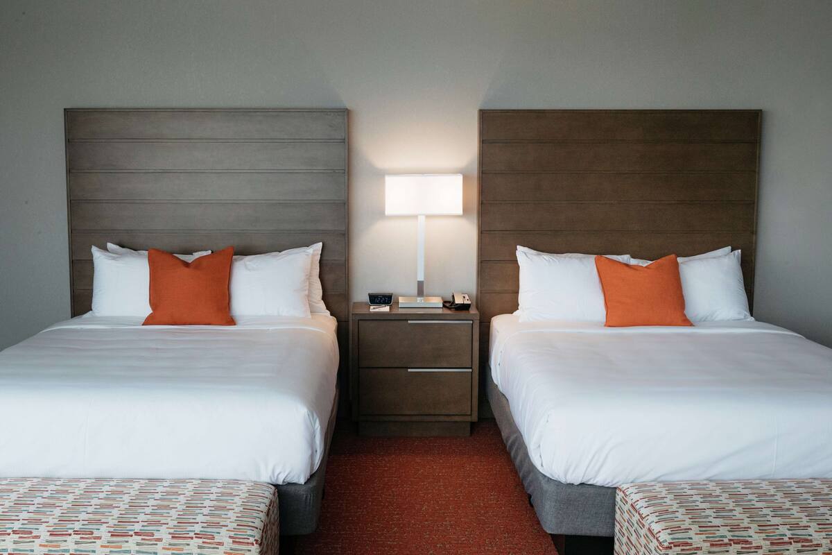 Ein Hotelzimmer mit zwei Betten, einem Nachttisch mit Lampe und einem roten Teppich.