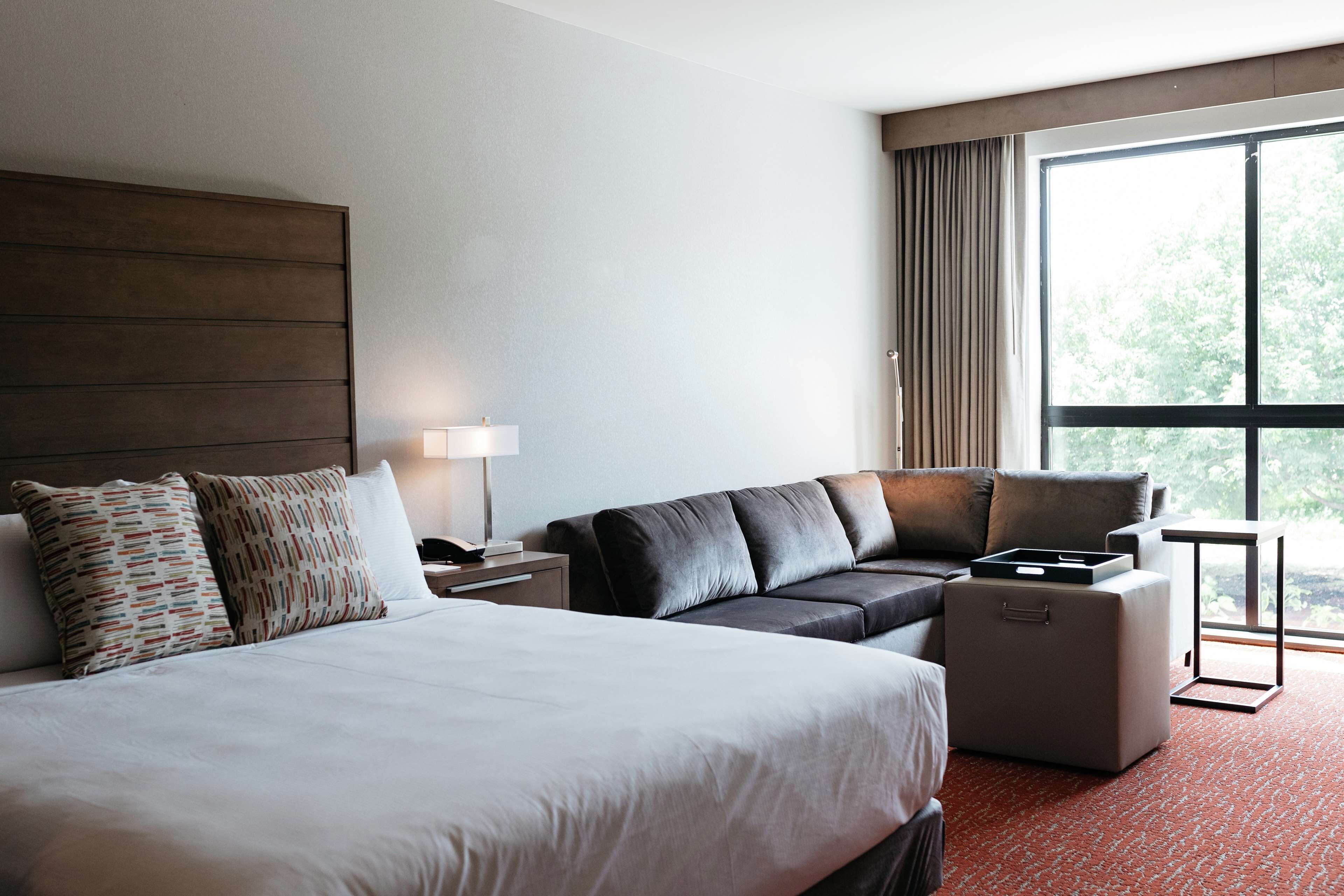 Ein Hotelzimmer mit einem großen Bett, einer Sitzecke, einem kleinen Tisch und einem Fenster mit Vorhängen.