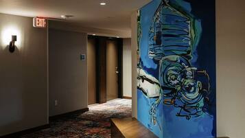 A hallway with an exit sign, a patterned carpet, and a large abstract painting on the wall.