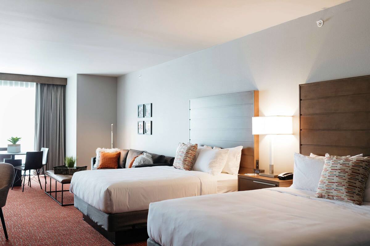 Ein Hotelzimmer mit zwei Betten, einem Schreibtisch, einem Stuhl, einer Lampe und einem kleinen Tisch mit einer Pflanze.