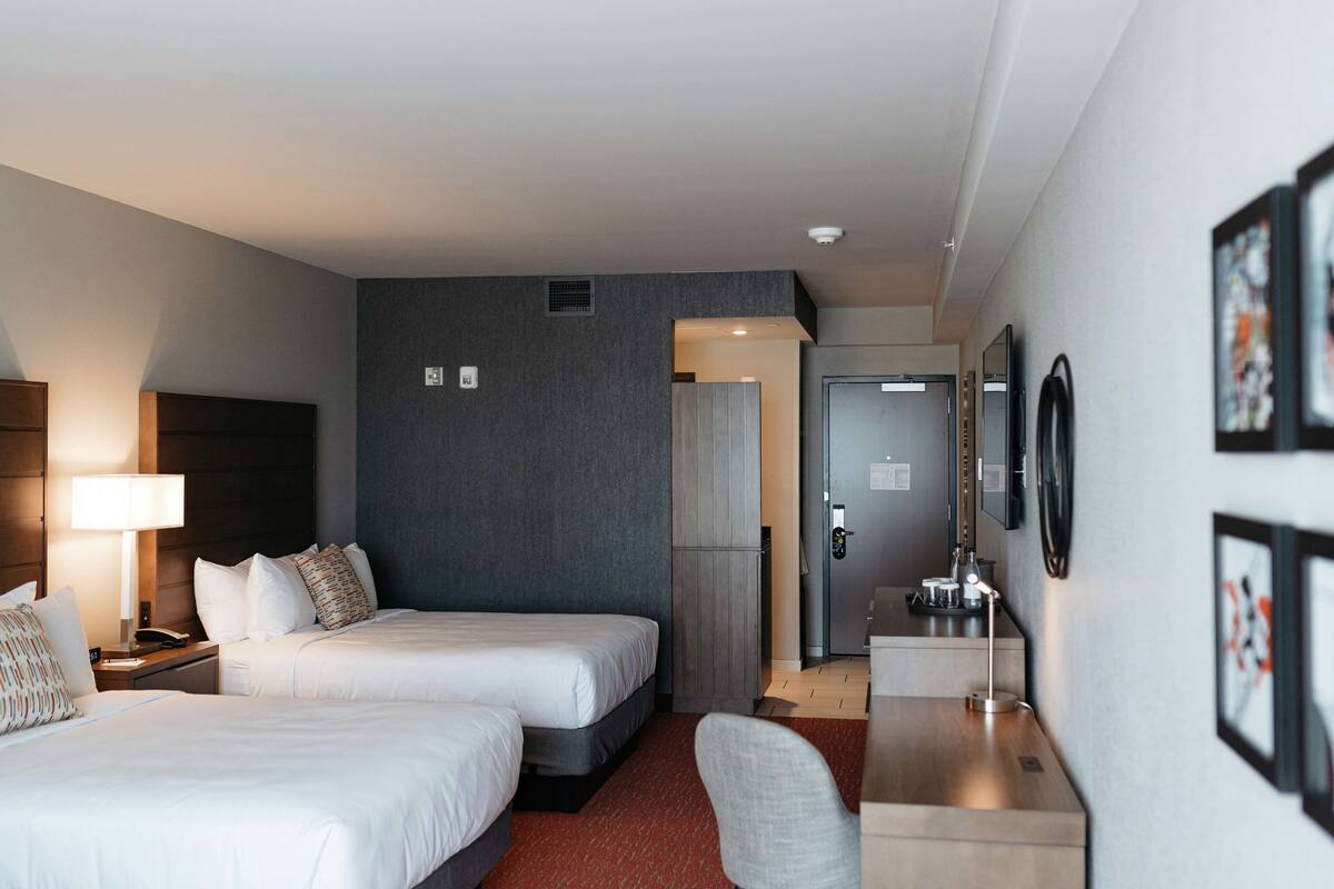 Ein Hotelzimmer mit zwei Betten, einem Schreibtisch, einem Stuhl, einem Kühlschrank und einem Spiegel.