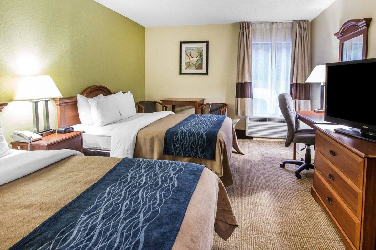A hotel room with two beds, a desk, a television, and a chair.