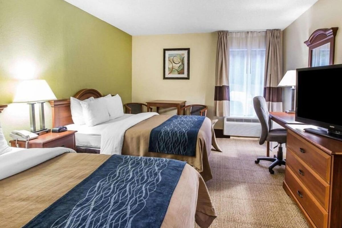 Habitación de hotel con dos camas, un escritorio, una silla, un televisor y una ventana con cortinas.