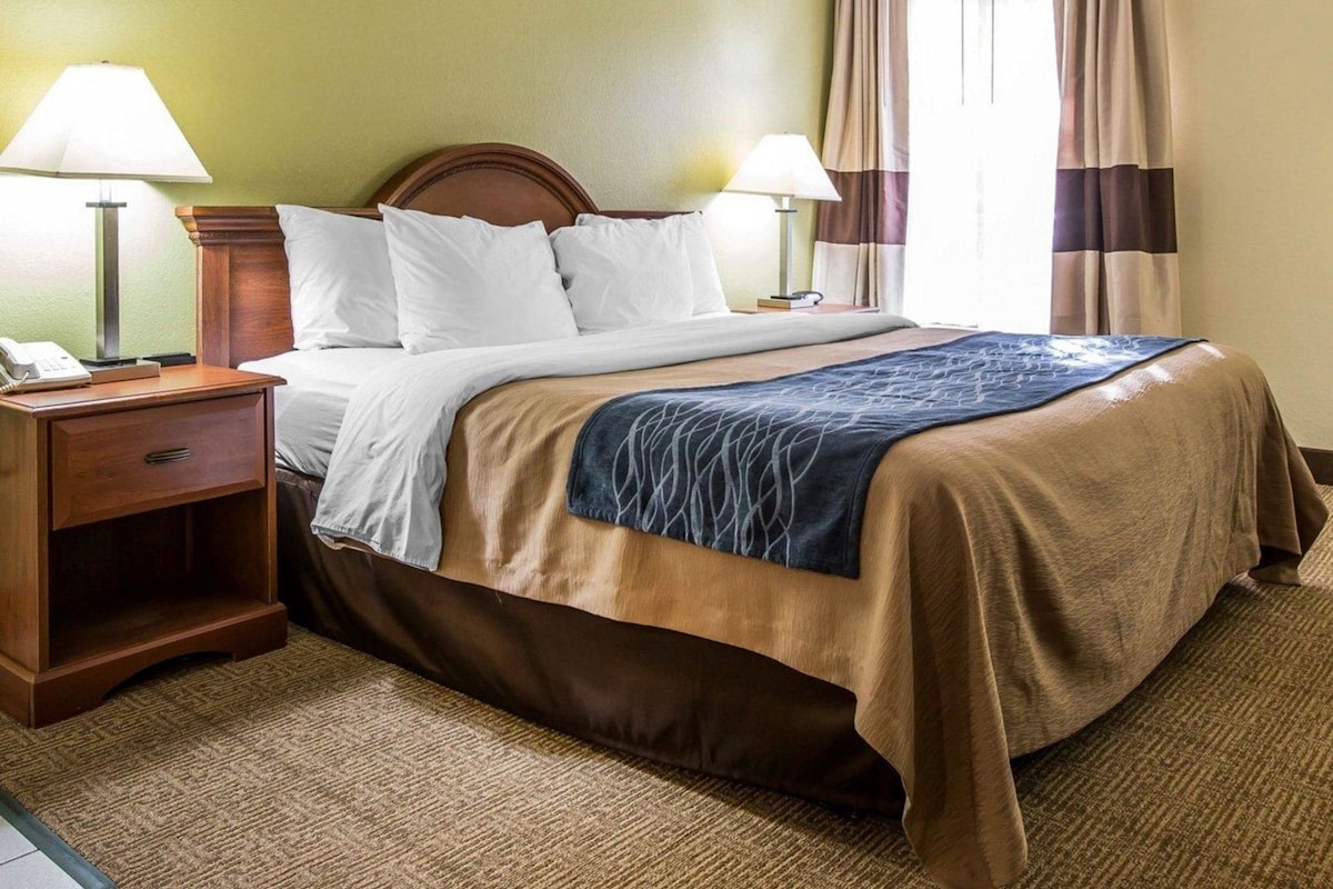Habitación de hotel con una cama, dos lámparas de noche, una mesita con un teléfono y una ventana con cortinas.
