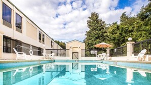 A swimming pool with lounge chairs and umbrellas, surrounded by a building with a gated entrance. - Quality Inn Darien - North Brunswick (Darien)