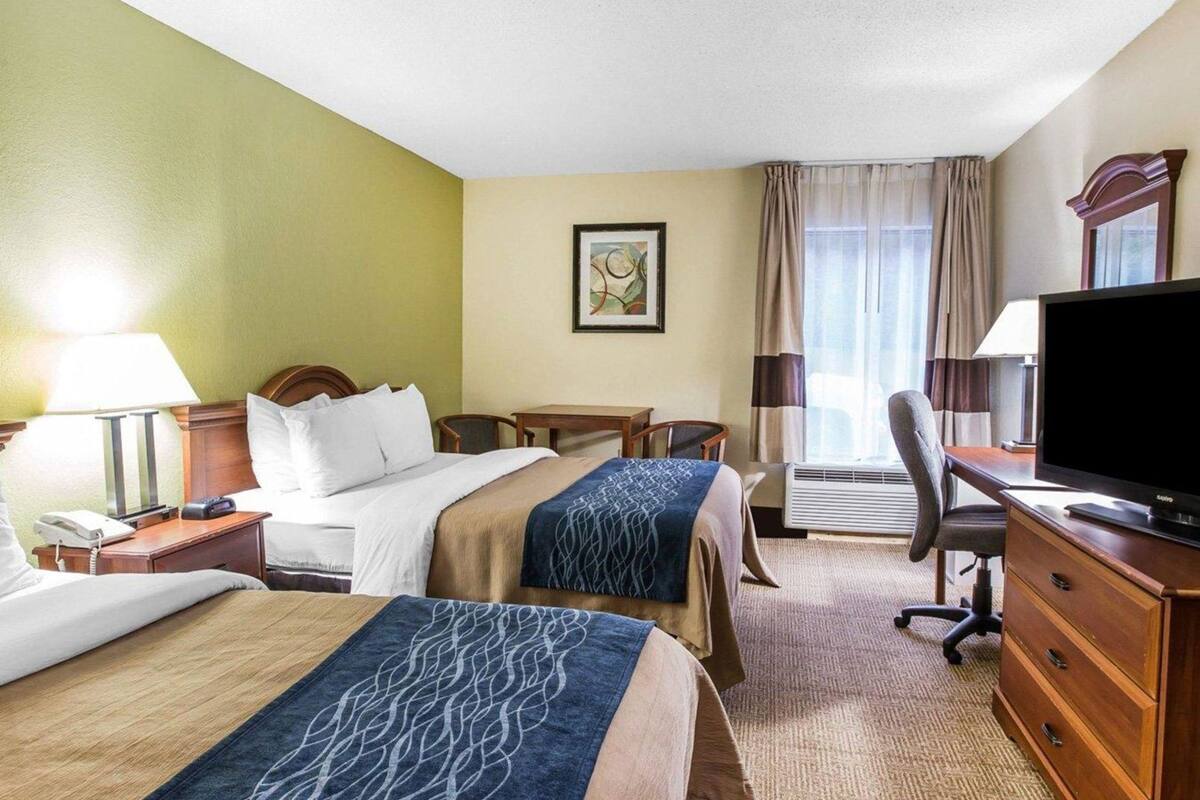 A hotel room with two beds, a desk, a chair, a television, and a window with curtains.