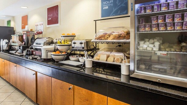 A breakfast bar with coffee machines, fruit bowls, and a refrigerated display of pastries and dairy products. - Quality Inn Darien - North Brunswick (Darien)