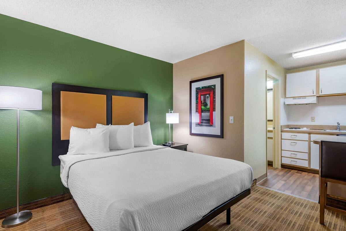 A hotel room with a bed, a desk, and a kitchenette.