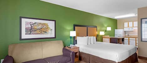 A hotel room with a green wall, a framed picture, a bed, a desk, a chair, a couch, and a small table.